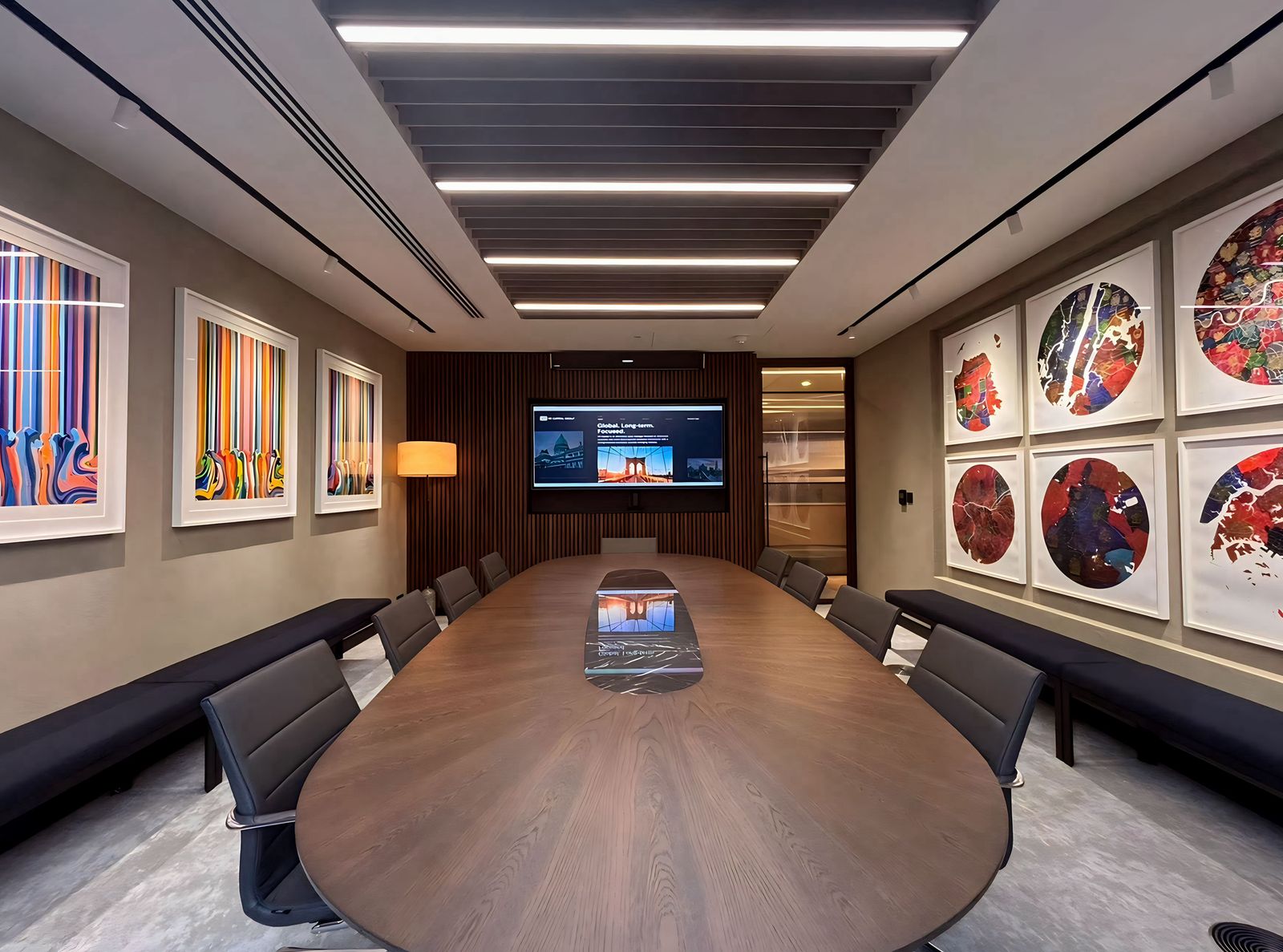 Boardroom with an oval timber table, video display and striped artwork on the walls