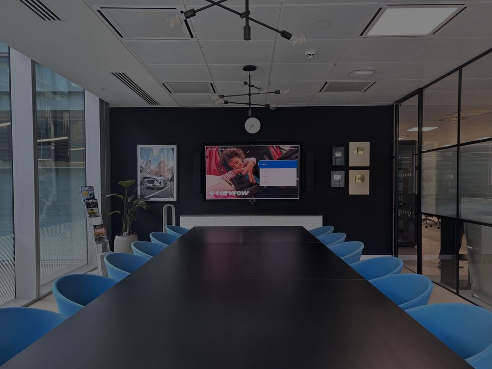 Long boardroom table with blue chairs facing a wall-mounted display at Carwow’s London HQ