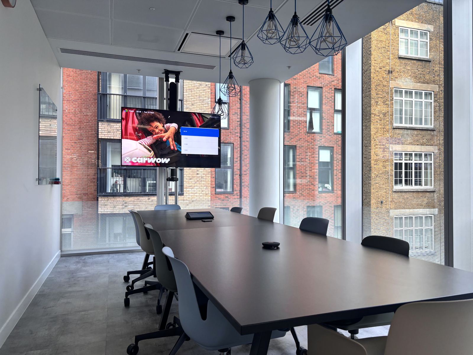 Corner meeting room at Carwow HQ with a ceiling-hung display above a dark meeting table