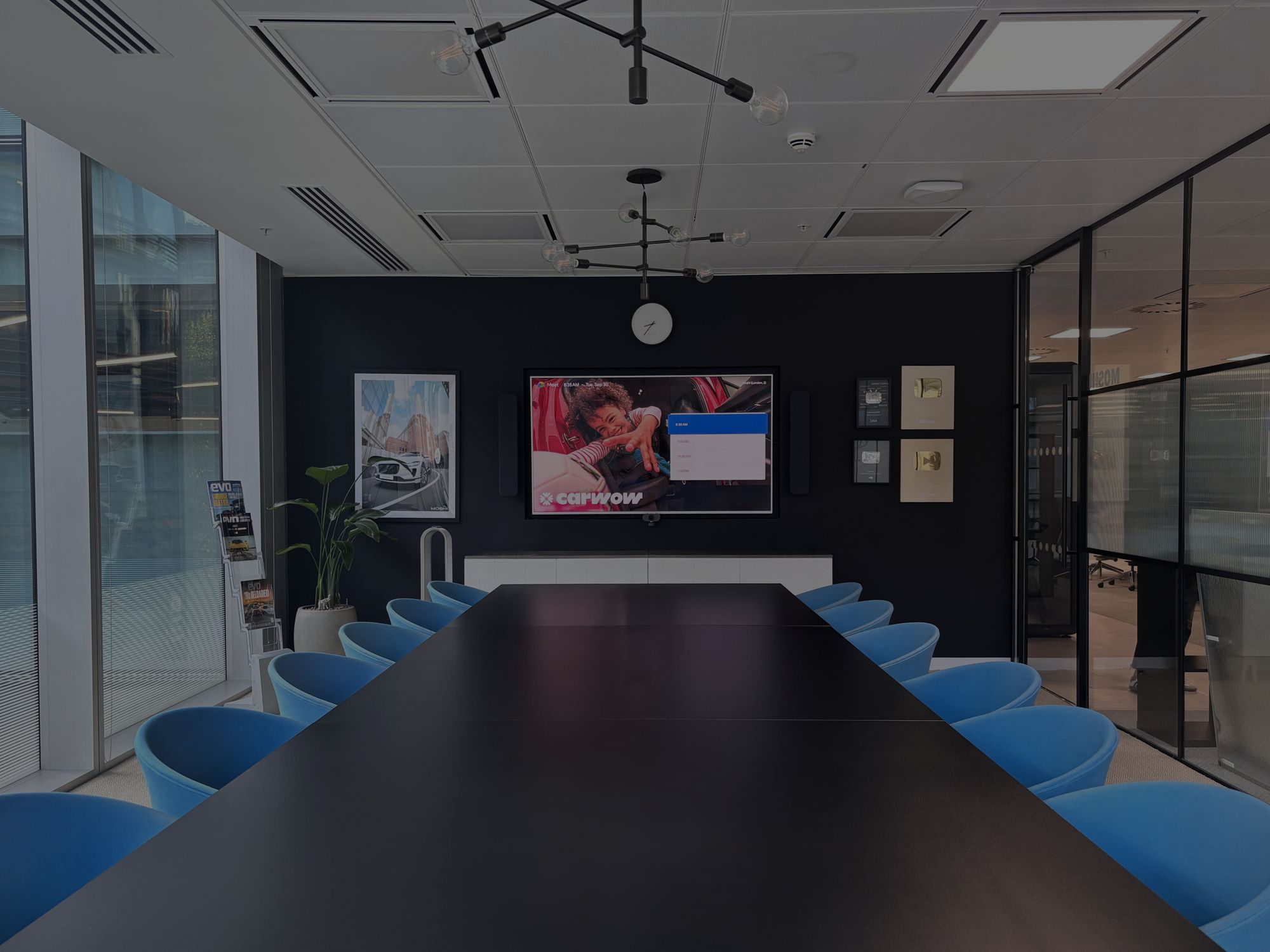 Long boardroom table with blue chairs facing a wall-mounted display at Carwow’s London HQ