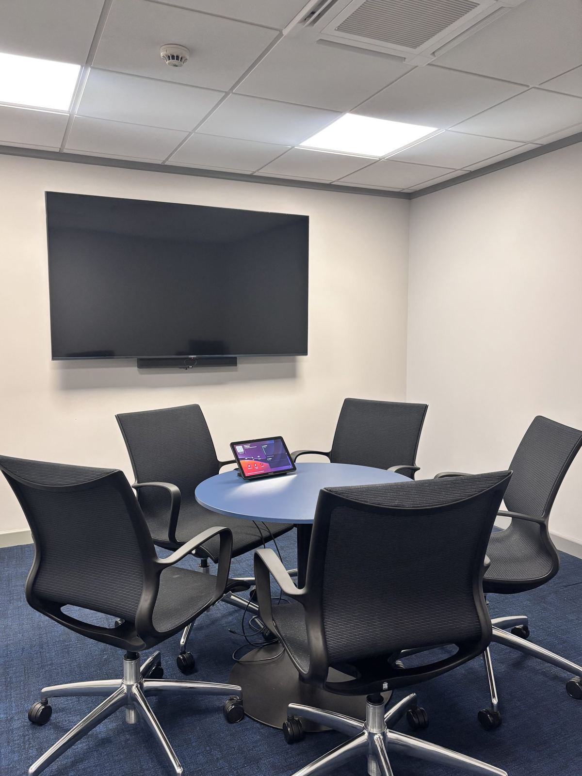 Menzies Aviation huddle room with a round table, wall display and touch panel