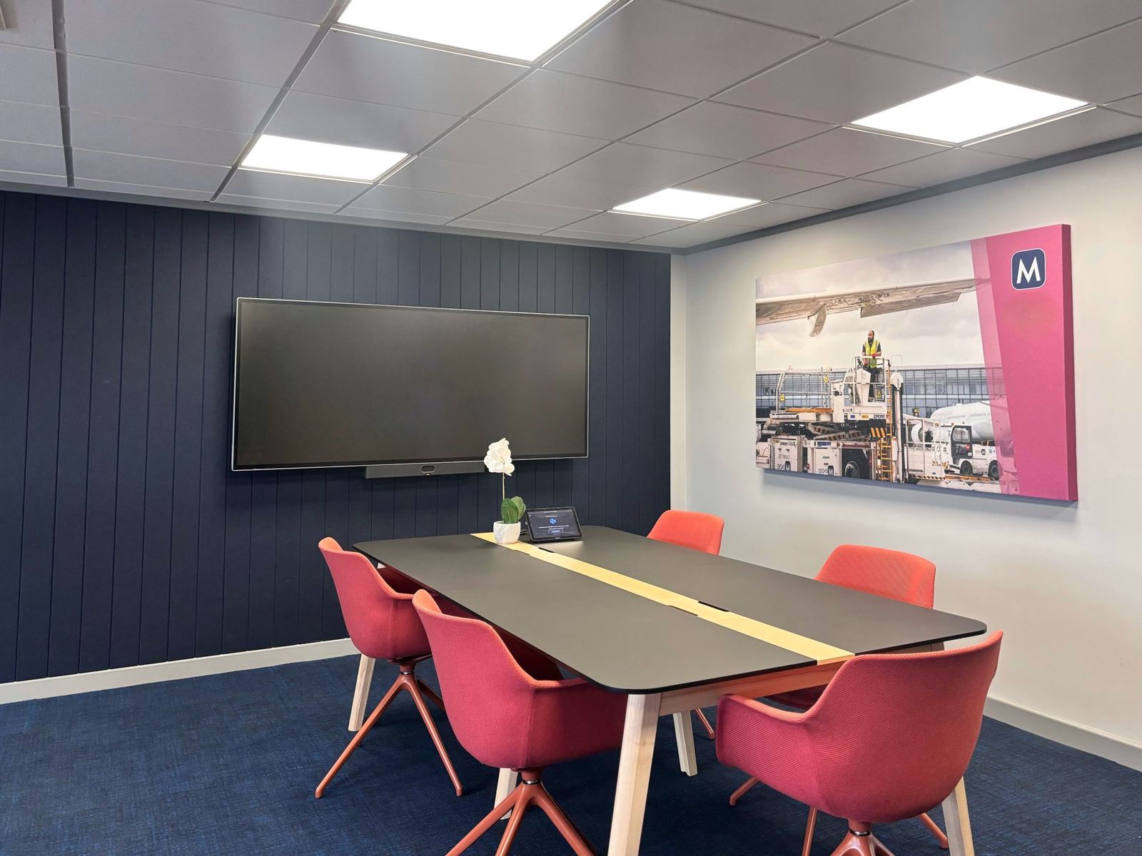 Menzies Aviation meeting room with red chairs, wall display and branded artwork